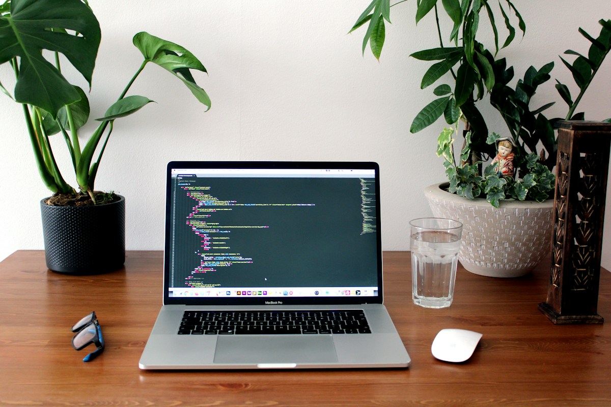 Laptop displaying software code on a desk with green plants